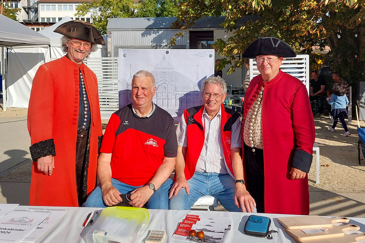 Zwei Vereinsmitglieder sitzen beim Salzfest. Zwei Halloren in ihrer traditionellen Tracht stehen links und rechts von ihnen.